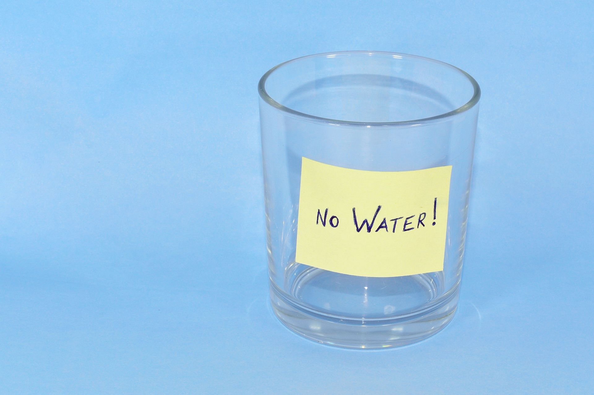 Empty Glass with a note saying No Water isolated on a blue background